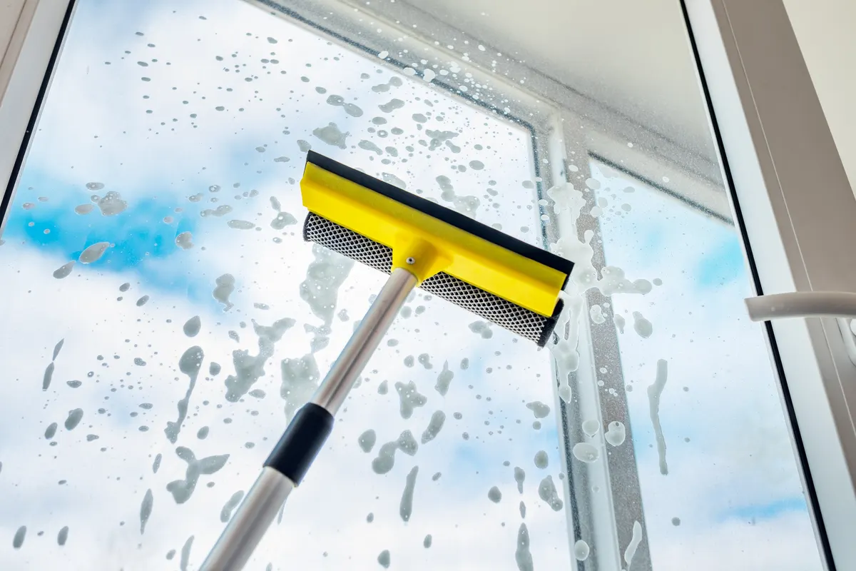 Fensterscheibe wird mit einem gelben Fensterwischer gereinigt, im Hintergrund blauer Himmel