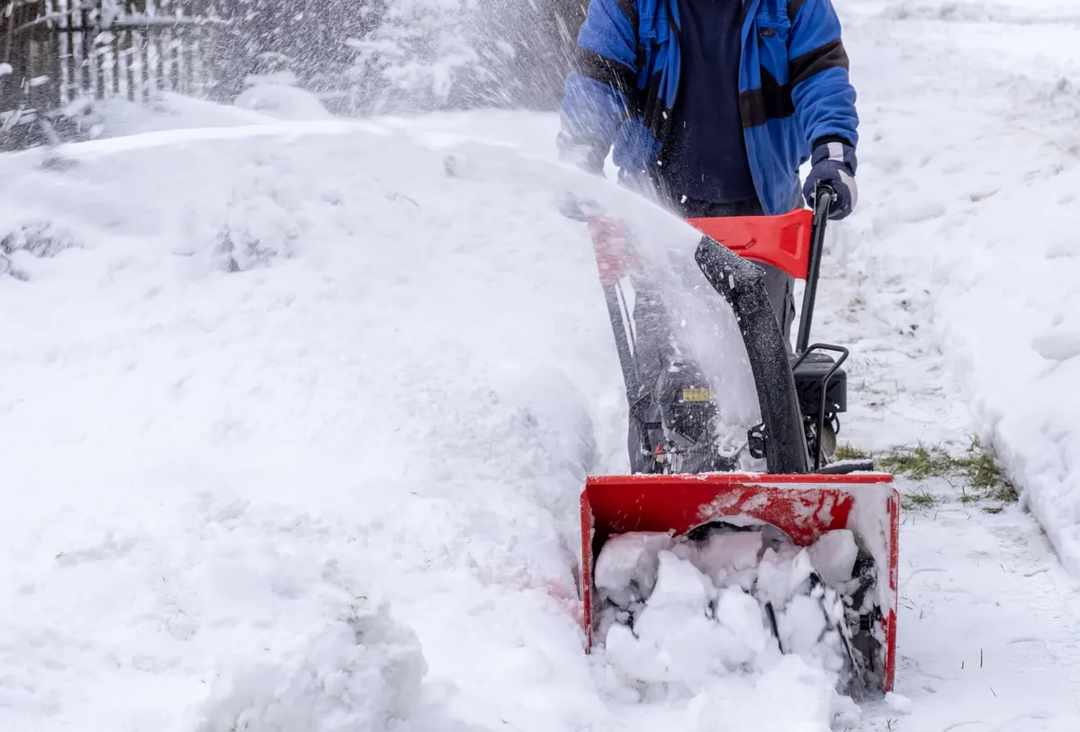 Mitarbeiter räumt mit einer Schneefräse einen verschneiten Hof