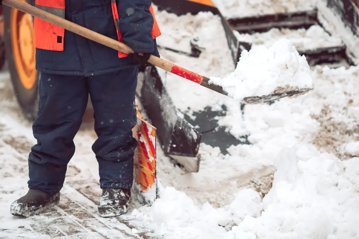 Winterdienst-Mitarbeiter schaufelt Schnee neben einem Räumfahrzeug